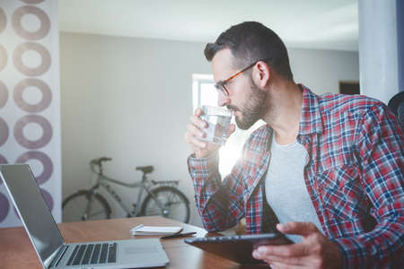 man drinking water and working with digital tablet pcの写真素材