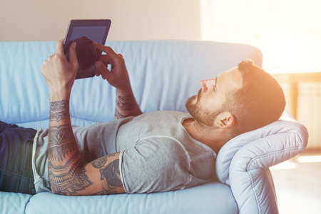 man lying on sofa with digital tablet pc at homeの写真素材