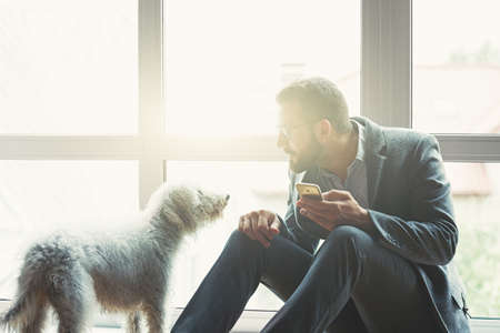 Handsome businessman with smart phone and cute dogの写真素材