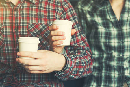 Couple in plaid shirts with two white paper cups of morning coffeeの写真素材