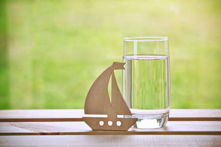 Glass of water with wooden sailing ship. Dreaming concept. Space for text