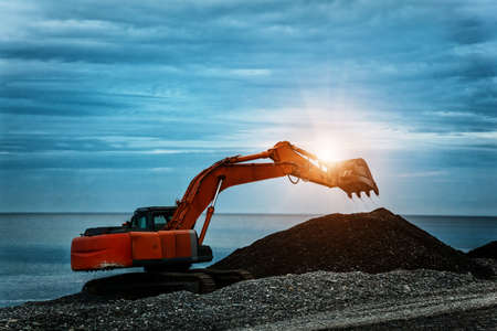 backhoe or digger working with bucket at industrial earth excavation site in sunrise light