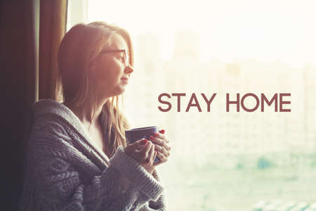 Pretty girl drinking coffee in morning and text Stay home. Home isolation and quarantine during...
