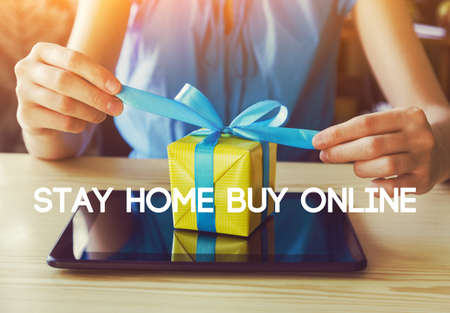 Hands with gift box and digital tablet. Text Stay home buy online. Home isolation and quarantine during coronavirus covid-19 pandemic.の写真素材