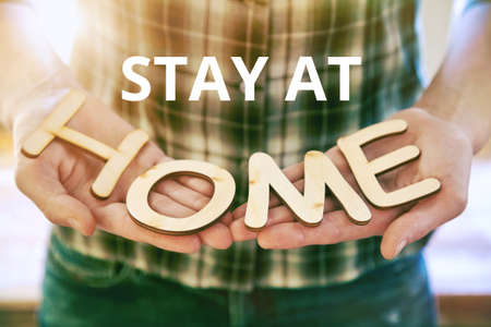 Hands holding wooden letters with word Home and text Stay at. Home isolation and quarantine during coronavirus covid-19 pandemic.の写真素材