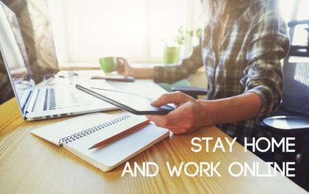 Hands with tablet, coffee and laptop at table and text Stay home and work online. Home isolation and quarantine during coronavirus covid-19 pandemic.の写真素材