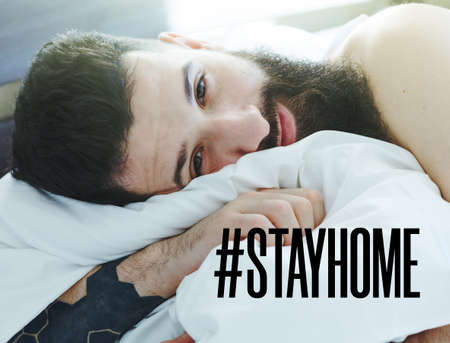 Bearded man lying in morning bed with text Stay home. Home isolation and quarantine during coronavirus covid-19 pandemic.の写真素材