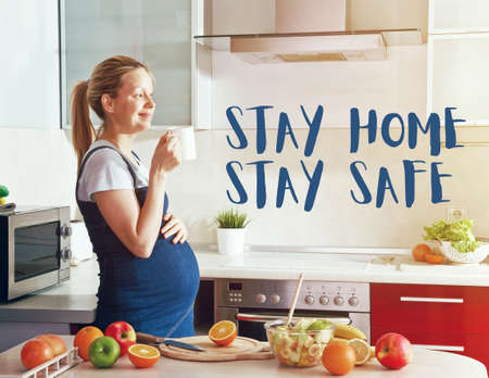 Pregnant woman on kitchen drinking juice or tea and text Stay home stay safe. Home isolation and quarantine during coronavirus covid-19 pandemic.の写真素材