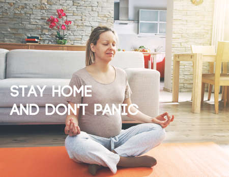 Pregnant woman practicing yoga and relaxing while sitting in lotus position.  Text Stay home and don't panic. Home isolation and quarantine during coronavirus covid-19 pandemic.の写真素材