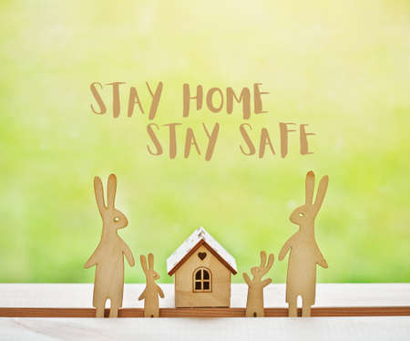 Family of wooden hares near house with text Stay at home, stay safe. Home isolation and quarantine during coronavirus covid-19 pandemic.の写真素材