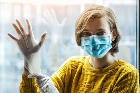 Woman in medical mask putting on gloves. Protection from catching disease or dirt. Pandemic of coronavirus concept.の写真素材
