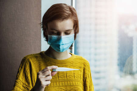 Portrait of woman holding thermometer checking temperature at home. Pandemic of coronavirus concept.の写真素材