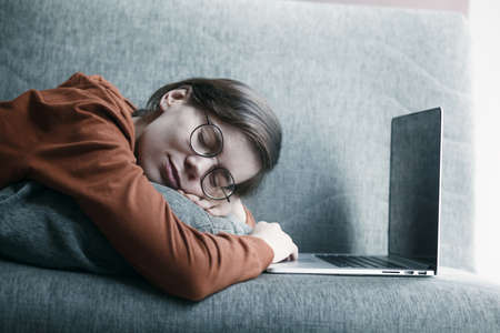 Woman sleeping and dreaming near laptop during working at home. Comfortable workplace lying on couch. Distance online educationの写真素材