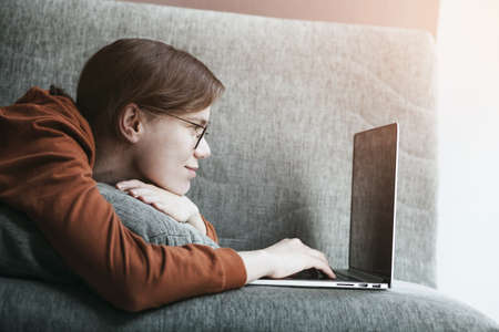 Woman working with laptop at home. Comfortable workplace lying on couch. Distance online educationの写真素材