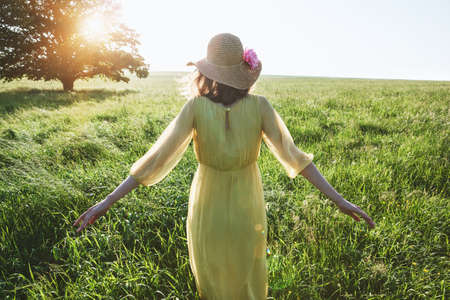 Pretty woman with yellow dress and hat walking in summer field in sunlghtの写真素材
