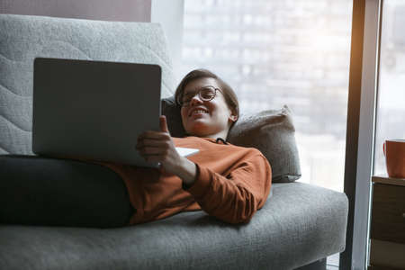 Woman working with laptop at home quarantine. Comfortable workplace lying on couch. Stay at home campaign.の写真素材
