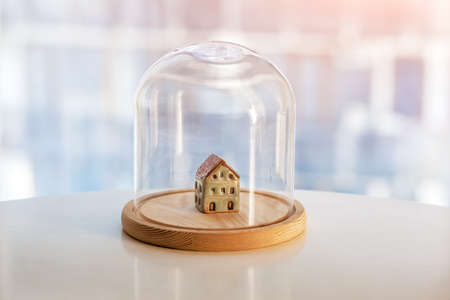 Ceramic model of house under glass cap. Symbol of safe home. Insurance or protecting building property concept.の写真素材