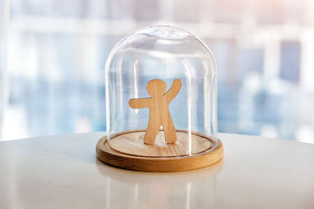 Wooden toy man under glass cap. Protecting life, personality and privacy concept. Symbol of keeping distance during pandemic or life mattersの写真素材