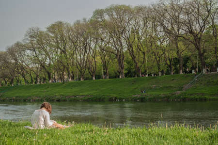 Girl in white on the river bank reading a book