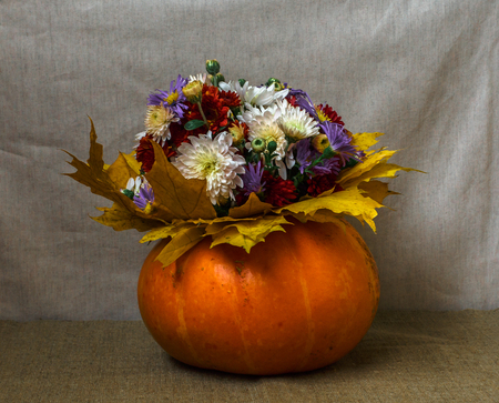 Pumpkin Vase with a bouquet of flowers and yellow leaves against the backdrop of a bright fabricの写真素材