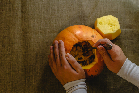 Pumpkin with top cut off. Hands of girl with a spoon take out the seeds from the pumpkin. View from aboveの写真素材