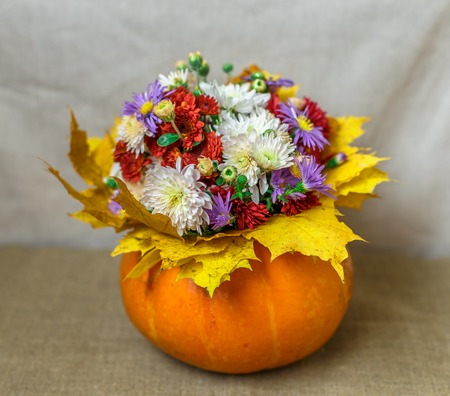 Pumpkin Vase with a bouquet of flowers and yellow leaves against the backdrop of a bright fabricの写真素材