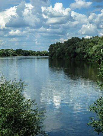 Natural river landscape with trees and white fluffy cloudsの写真素材