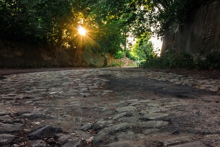 Old road from stone blocks. Rays of the setting sun shining through the treesの写真素材