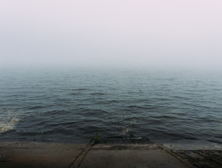 Thick morning fog on the lake. The beach of concrete slabs in the foregroundの写真素材