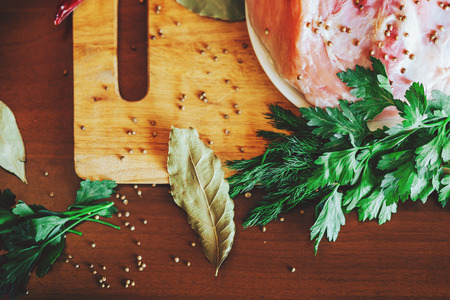 Raw meat on cutting board with green vegetables, red pepper, Bay leaf, spices on a kitchen wooden table. Macro, top view, close up.の写真素材
