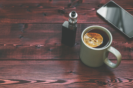 tea cup, mobile phone and electronic cigarette for vaping on wood table background. time for relax