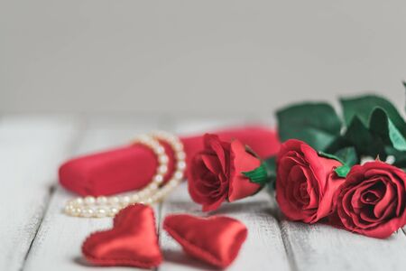 Valentines Day background with roses, gift box with bead and two red fabric hearts on wooden background. Copy spaceの写真素材