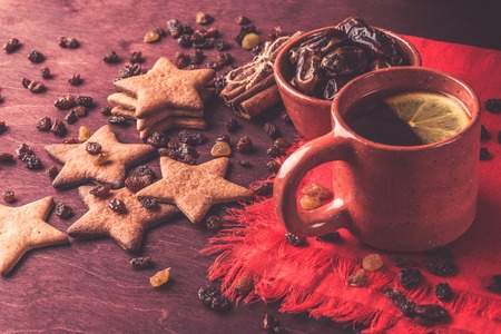 Homemade ginger cookies, cup of tea with lemon, dates, cinnamon with raisins on a red wooden table....