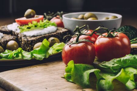 Vegetarian and healthy food concept. Tomatoes and Sandwiches of homemade bread with cheese sauce or cream, lettuce, tomatoes, olives in a bowl. Healthy breakfast or snack on wooden board.の写真素材