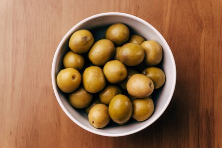 Fresh green olives in white bowl on wooden table background. Top view.の写真素材