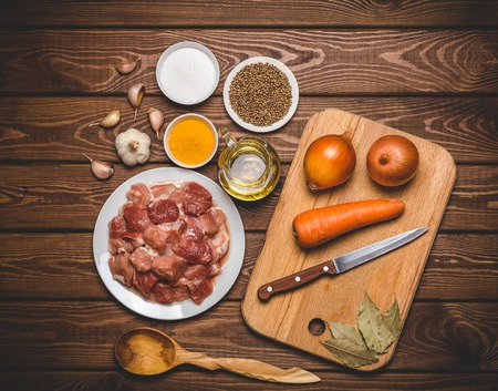 Cooking ingredients: sliced raw meat, oil, spices, garlic, carrot, onion, bay leaf and parsley, cutting board on wooden rustic table. Top viewの写真素材