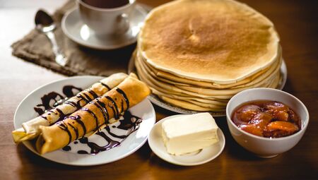 Stack of delicious homemade pancakes or blini with chocolate, cup of tea, butter and jam in a bowl...