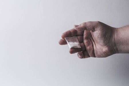 Mans hand holds plastic packet with cocaine powder or another drugs. Drug dealer selling drugs junkie. Free copy space for textの写真素材