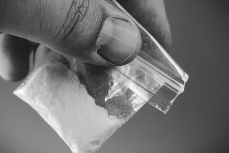 Mans hand holding or giving plastic packet with portion of cocaine or another drugs. Problems with drugs concept. Black and white photoの写真素材