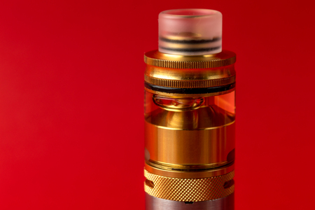 Vaping device, rebuildable atomiser with e-liquid or e-juice of glycerin on red background. Vape...