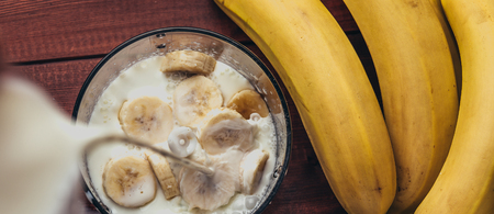 Panoramic image of preparation banana smoothie, pouring milk in a blender over pieces of banana for shaking, healthy food conceptの写真素材