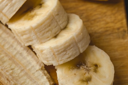 Macro photo of Cut into slices banana on a wooden cutting board, top viewの写真素材