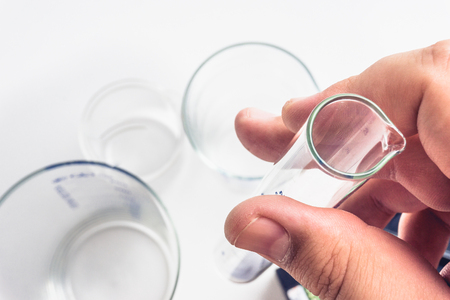 Male hand holds a test tube, against a background of flasks, beakers, laboratory equipment, top view on a white backgroundの写真素材