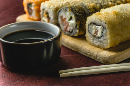 Close up of sushi rolls set served on wooden dish with soy sauce and chopsticks on dark red background, copy spaceの写真素材