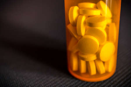 Close-up of pills or medication tablets in an orange pill bottle standing on a black table, copy...