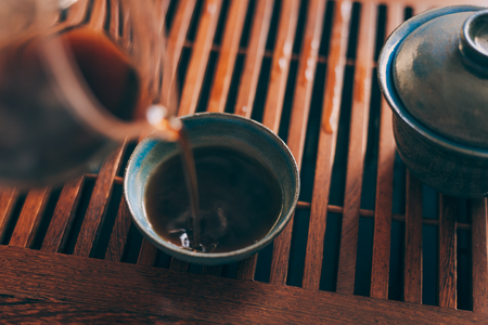 Chinese tea cup is poured by hot fresh black tea of Shu Puer or Puerh on Chinese tea board, selective focusの写真素材