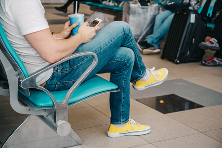 Young man using smartphone and seating on chair in waiting airport area, waiting for flight at airportの写真素材