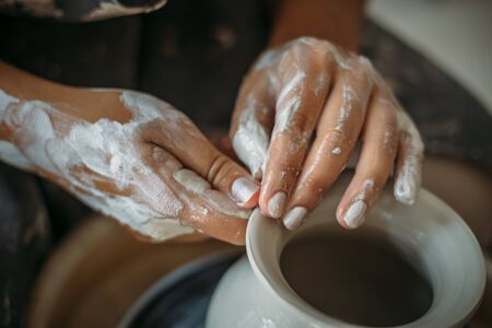 Dirty hands in white clay, pottery wheel with bowl or jar. Potter at work, woman's hands, selective...