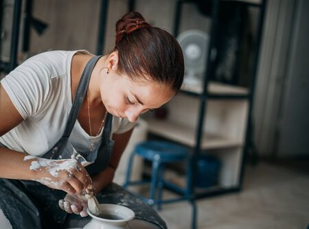 Female potter at work at pottery wheel in workshop, creating bowl from white clay, copy space