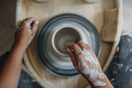 Top view of dirty potter woman hands works at pottery wheel, potter makes new ceramic production,...